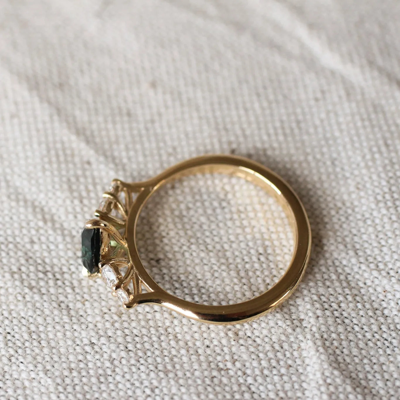 top view displaying high-set collet of pear sapphire and diamond engagement ring on a beige fabric