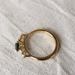 top view displaying high-set collet of pear sapphire and diamond engagement ring on a beige fabric