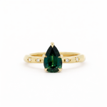 Gold engagement ring with a green pear sapphire and star set diamonds on a white background