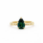 Gold engagement ring with a green pear sapphire and star set diamonds on a white background