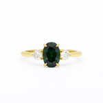 blue green oval engagement ring with round diamonds and gold band on a white background