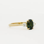 side view of a 18ct gold engagement ring with round diamonds and oval blue/green sapphire on a white background