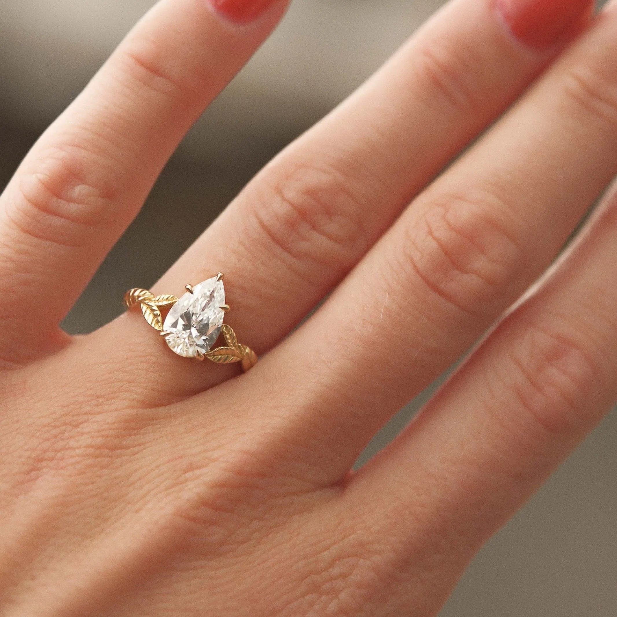 Gold ring with a diamond on a hand with red nail polish against a blurred background