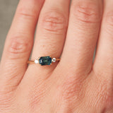 Close-up of a hand wearing a ring with a green gemstone on a neutral background