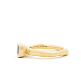 A gold ring with a textured, organic-shaped band and a small oval blue gemstone, shown in profile against a solid white background.