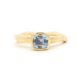 A gold ring with a wavy, organic-shaped band and a square bezel-set light blue gemstone, shown on a clean white background.