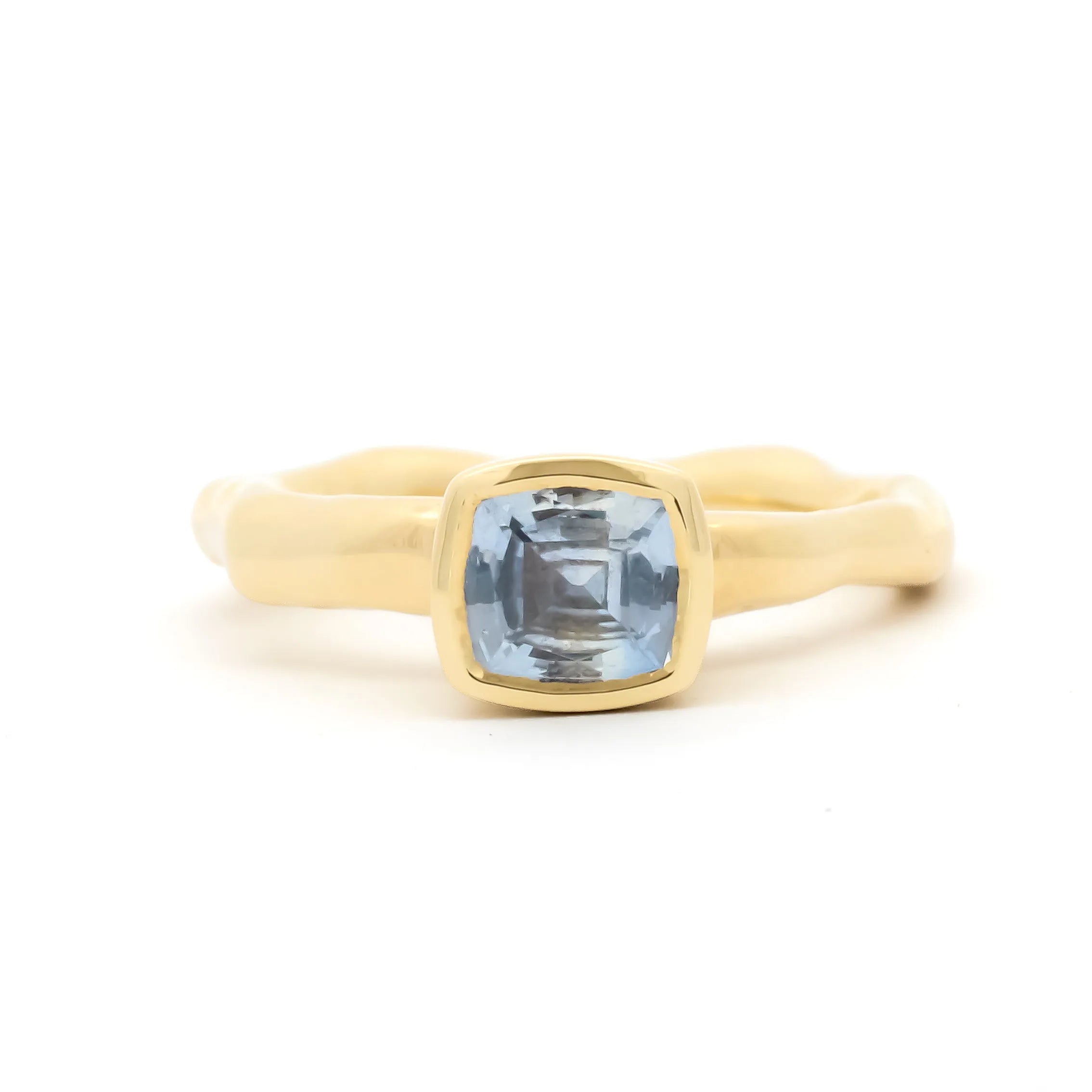 A gold ring with a wavy, organic-shaped band and a square bezel-set light blue gemstone, shown on a clean white background.