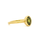 side view of a bezel oval sapphire engagement ring with satin finish gold on a white background