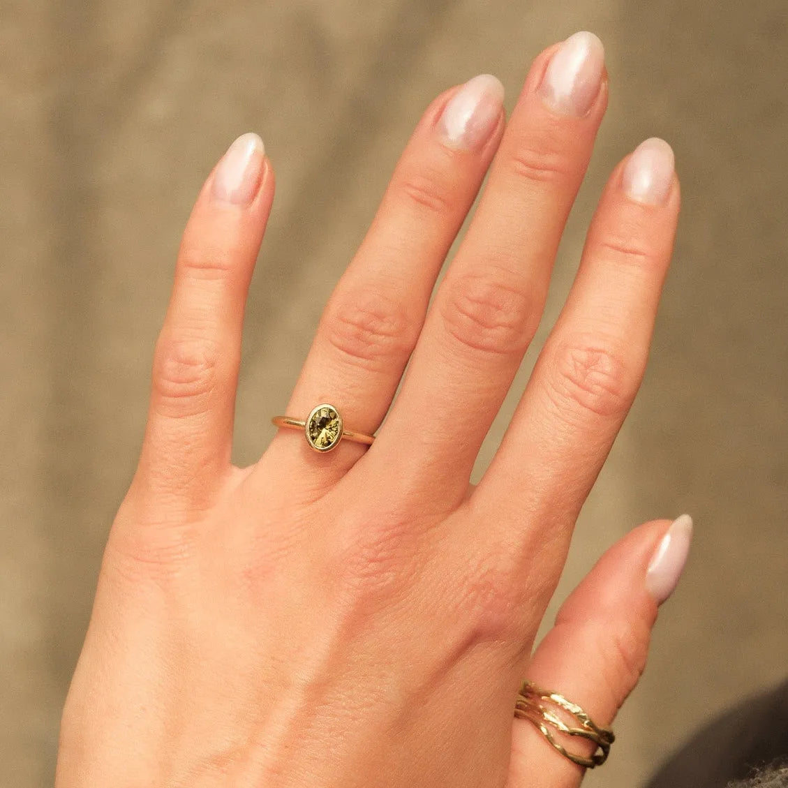 hand wearing oval green sapphire bezel engagement ring with shadows