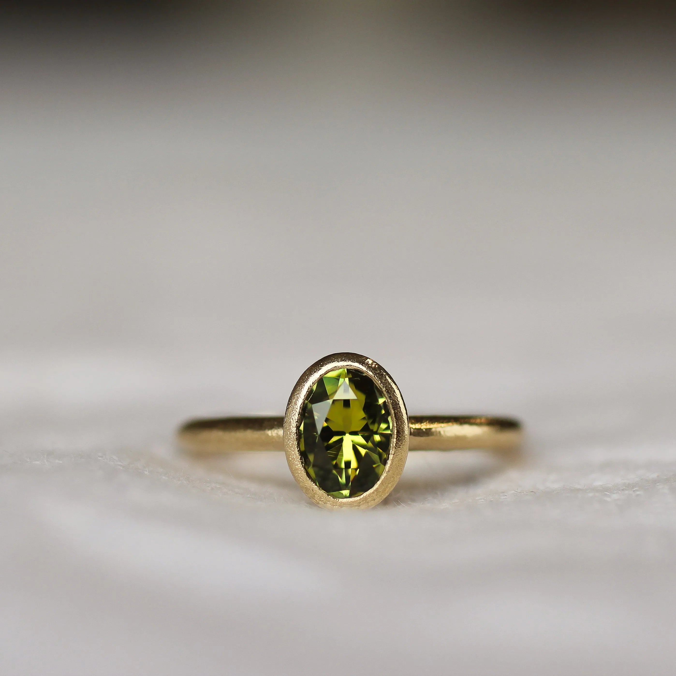 Bezel Solitaire Green/Yellow Sapphire Engagement Ring with Satin Finish on a neutral fabric