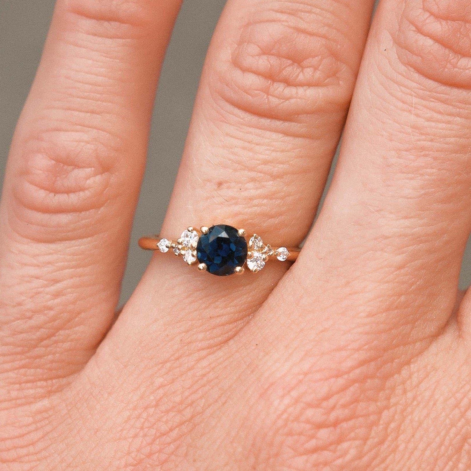 Close-up of a hand wearing a ring with a blue gemstone on a neutral background