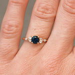 Close-up of a hand wearing a ring with a blue gemstone on a neutral background
