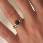 gold ring with a blue gemstone and curved wedding ring worn on a hand against a neutral background
