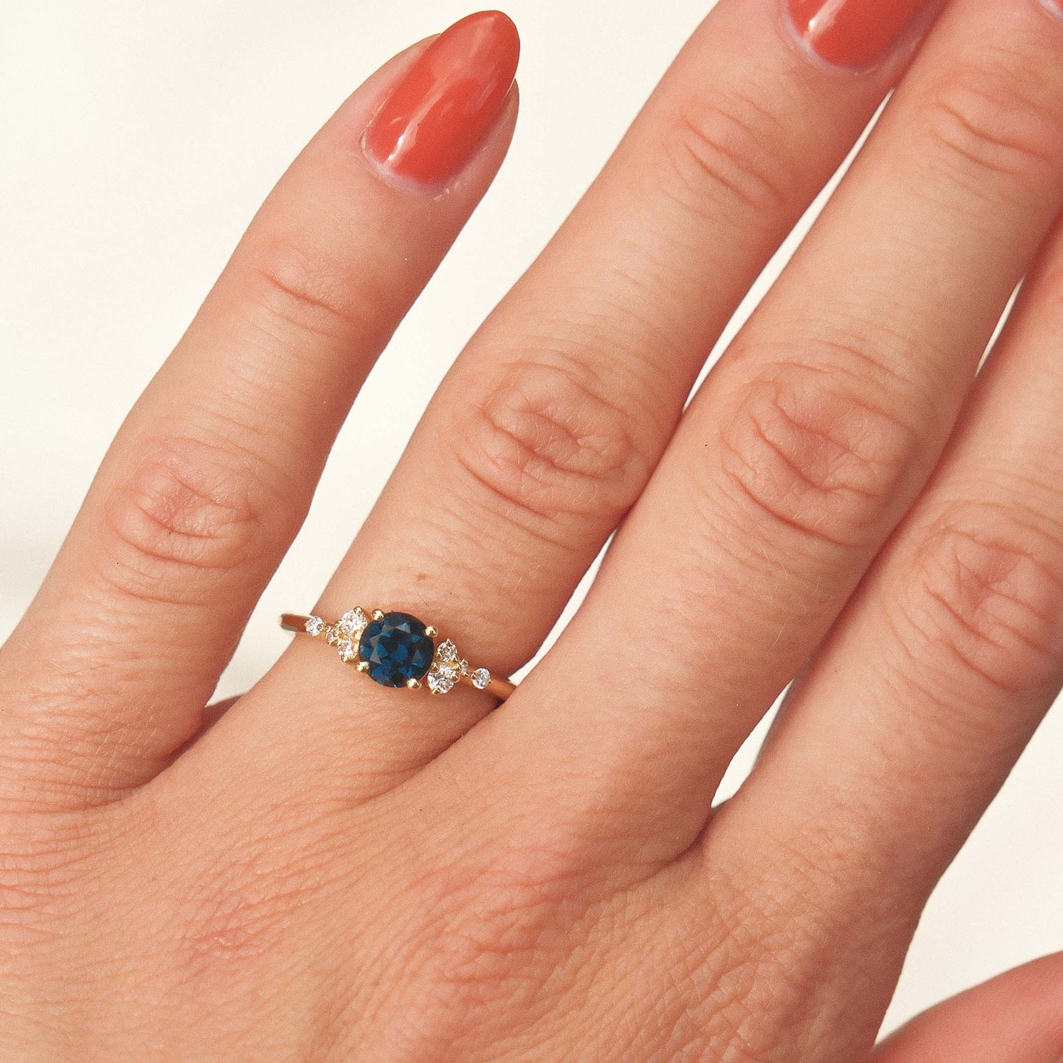 Hand wearing a ring with a blue gemstone on a plain background