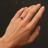 Hand wearing a blue sapphire organic engagement ring against a dark background