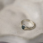 white gold engagement ring with a blue oval sapphire and organic texture on a ceramic beige surface