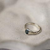 white gold engagement ring with a blue oval sapphire and organic texture on a ceramic beige surface