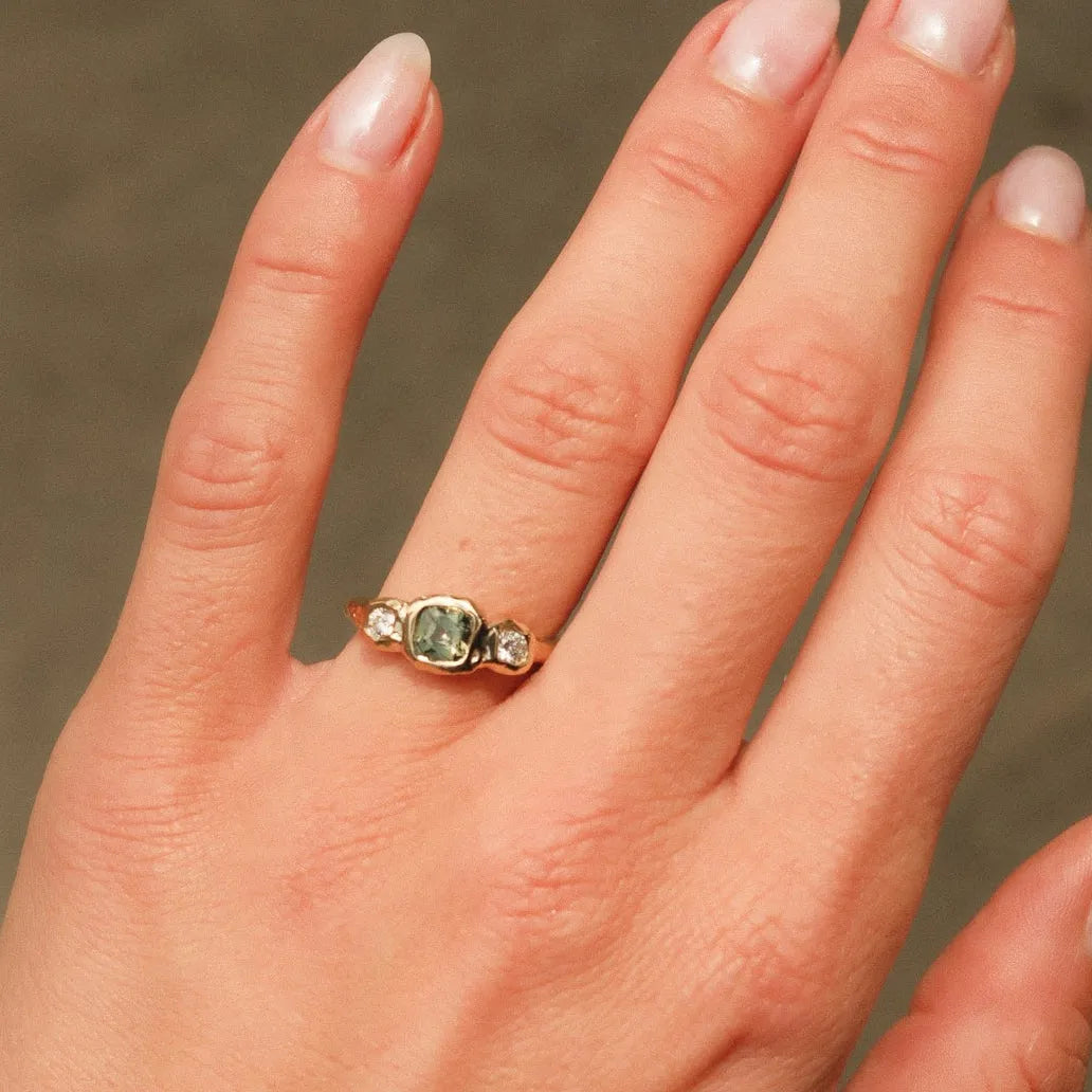 Hand wearing a ring with a green gemstone against a neutral background