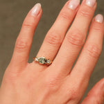 Hand wearing a ring with a green gemstone against a neutral background