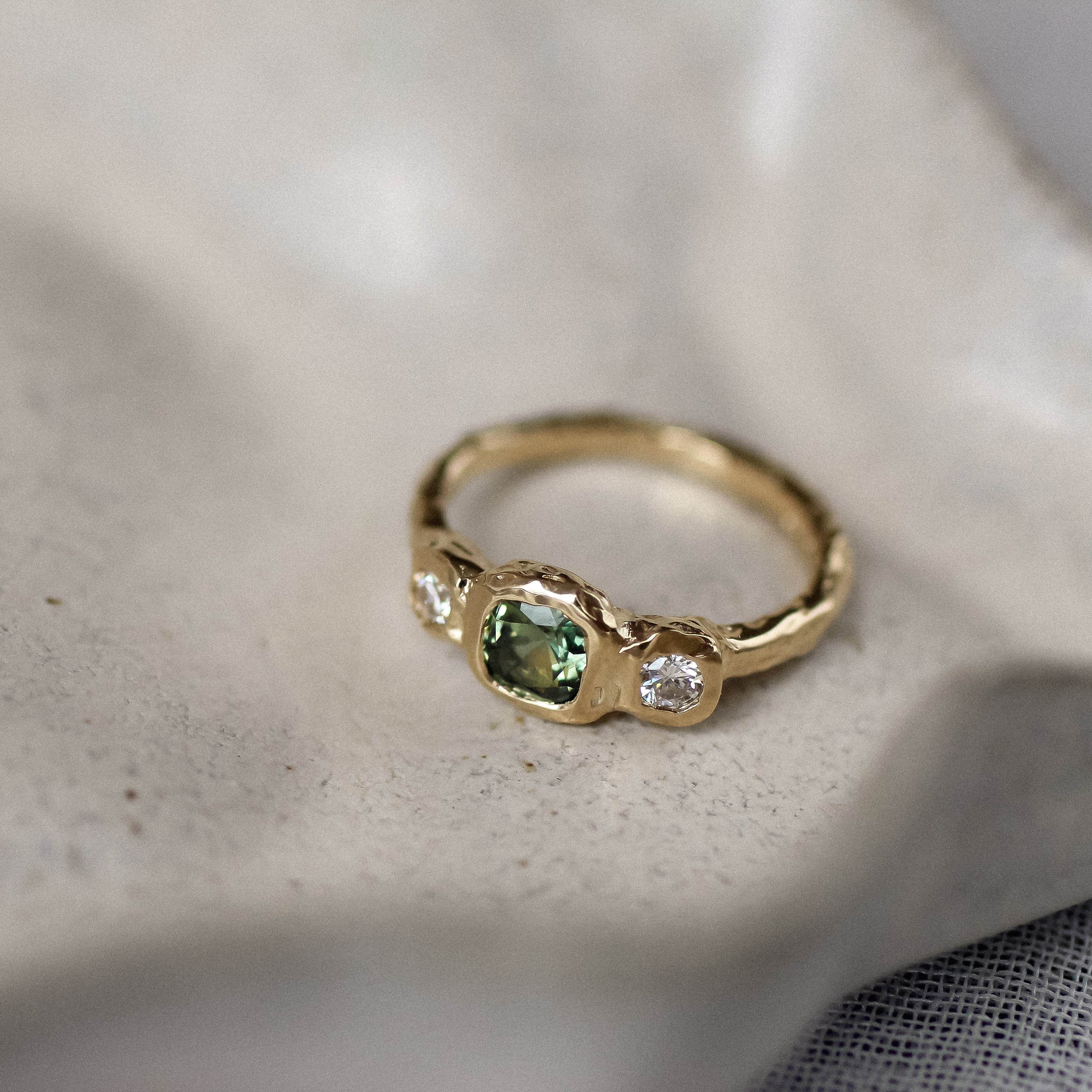Gold ring with green gemstone on a textured surface