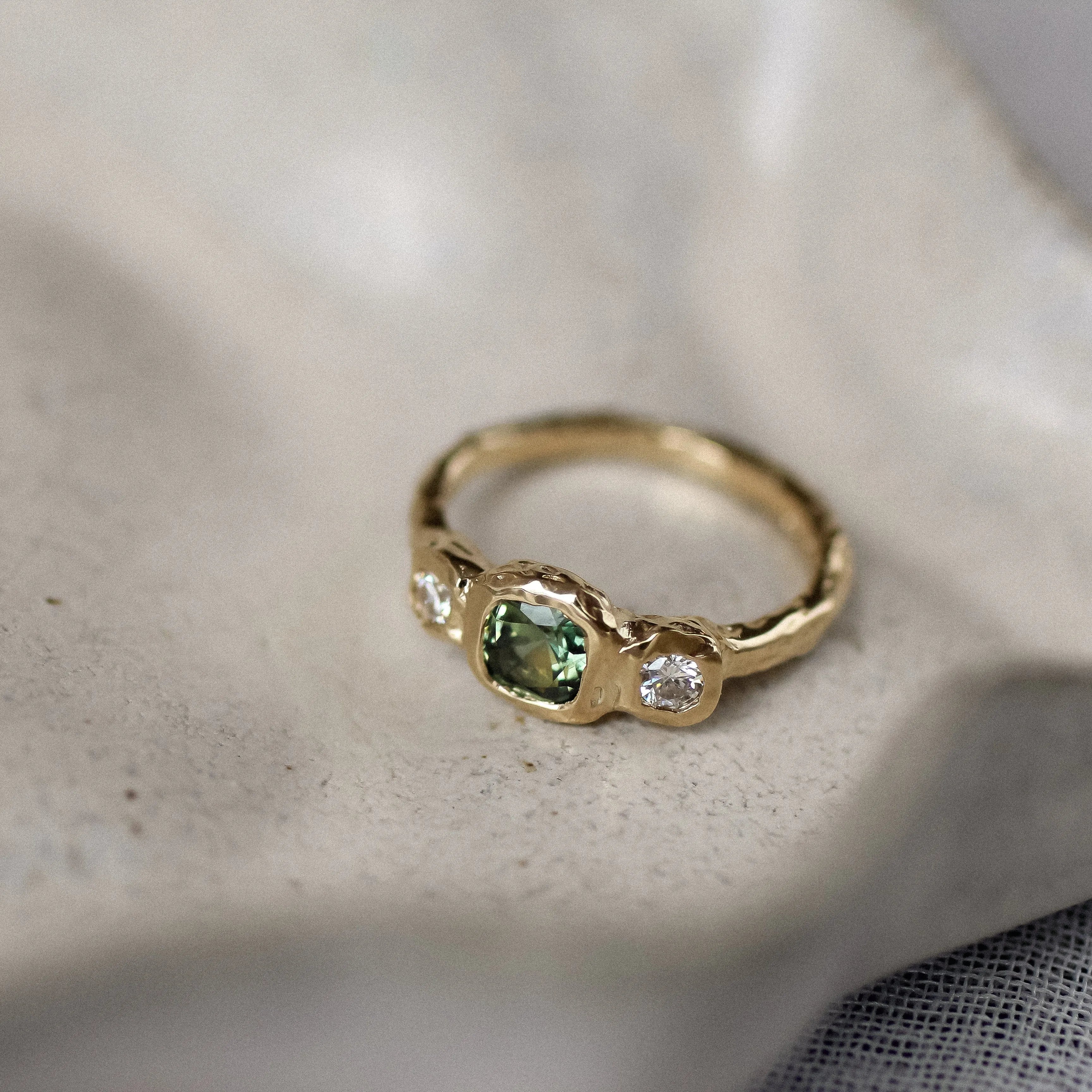 Gold ring with green gemstone on a textured surface
