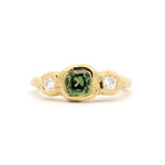 molten bezel engagement ring with cushion cut green sapphire and round diamonds on a white background