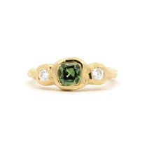 molten bezel engagement ring with cushion cut green sapphire and round diamonds on a white background