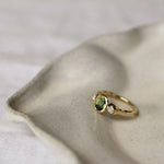 gold textured molten ring with a green oval sapphire and round diamonds on a textured beige surface