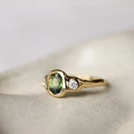 Oval Green Sapphire and Diamond Molten Organic Engagement Ring on a ceramic surface