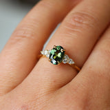 Gold ring with a green oval sapphire and round and pear diamond accent stones on a person's finger