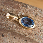 Gold pendant with a blue gemstone on a textured surface