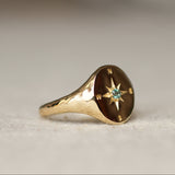 Gold ring with compass design and gemstone on a light background