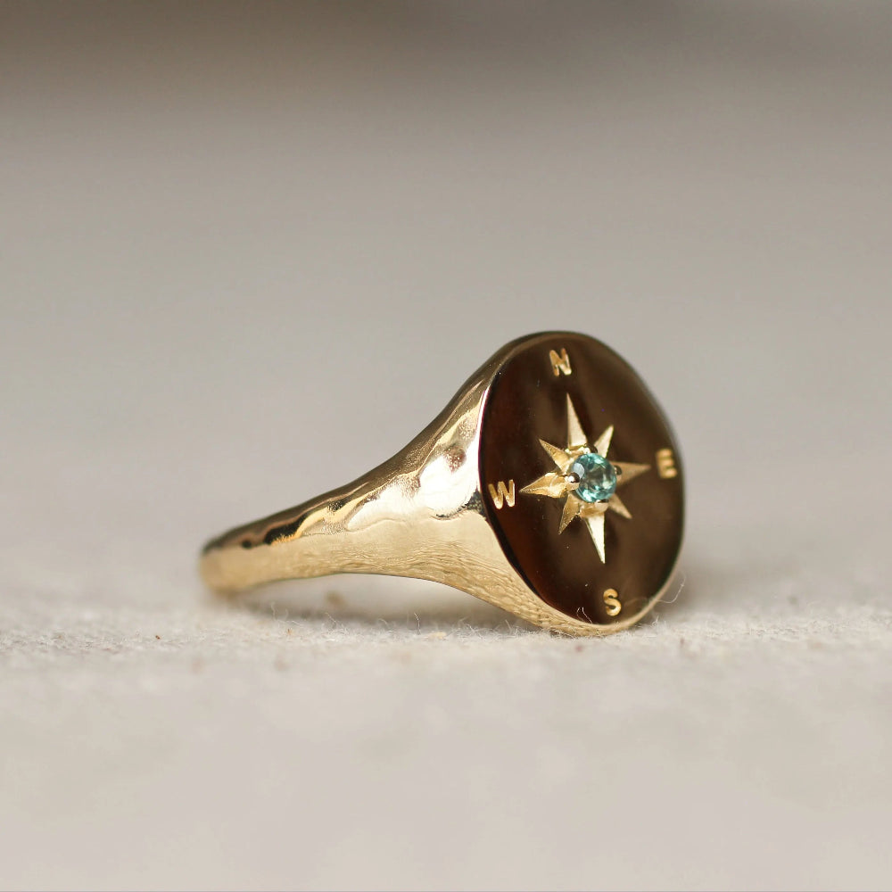 Gold ring with compass design and gemstone on a light background