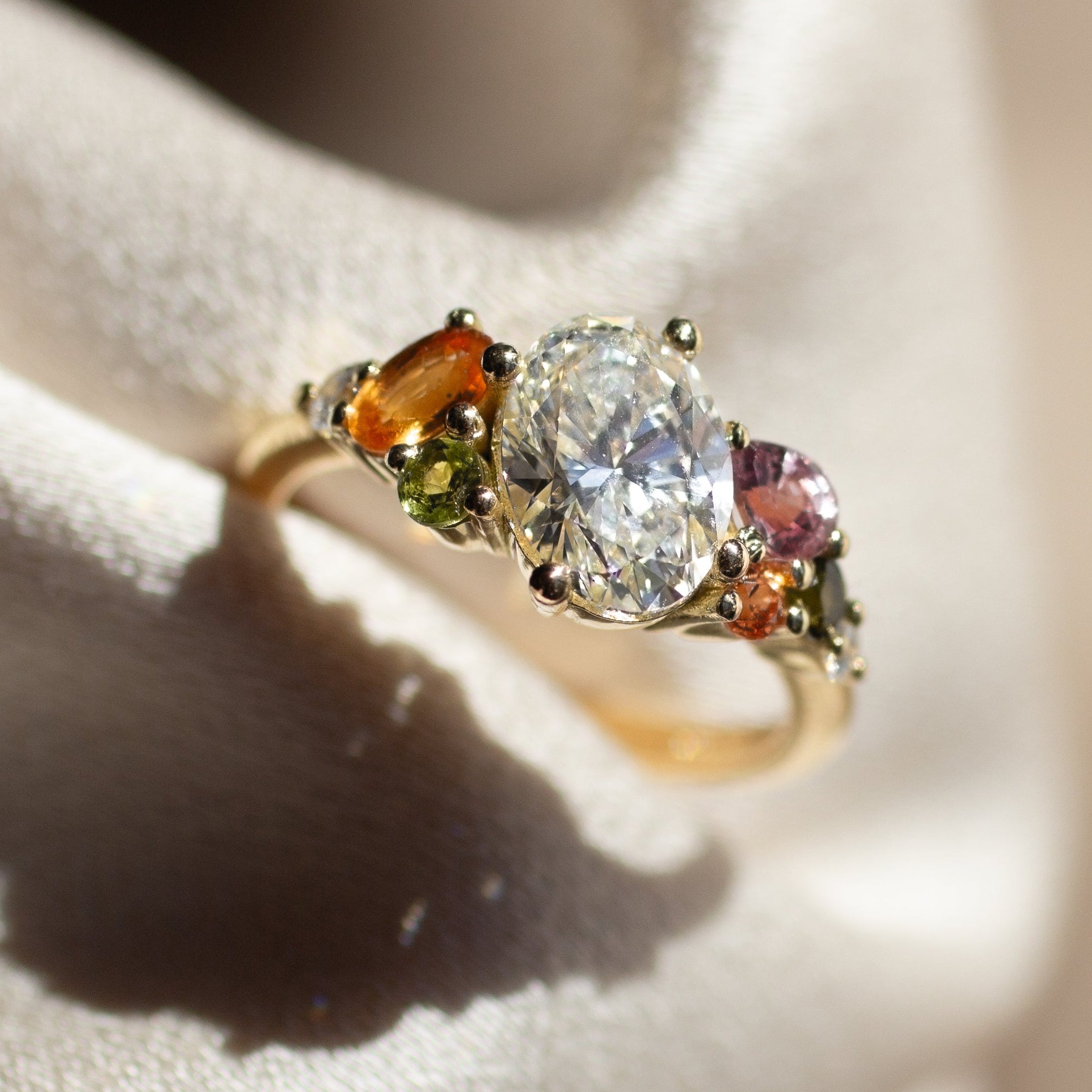 bespoke engagement ring with oval diamond and pink, orange and green sapphires