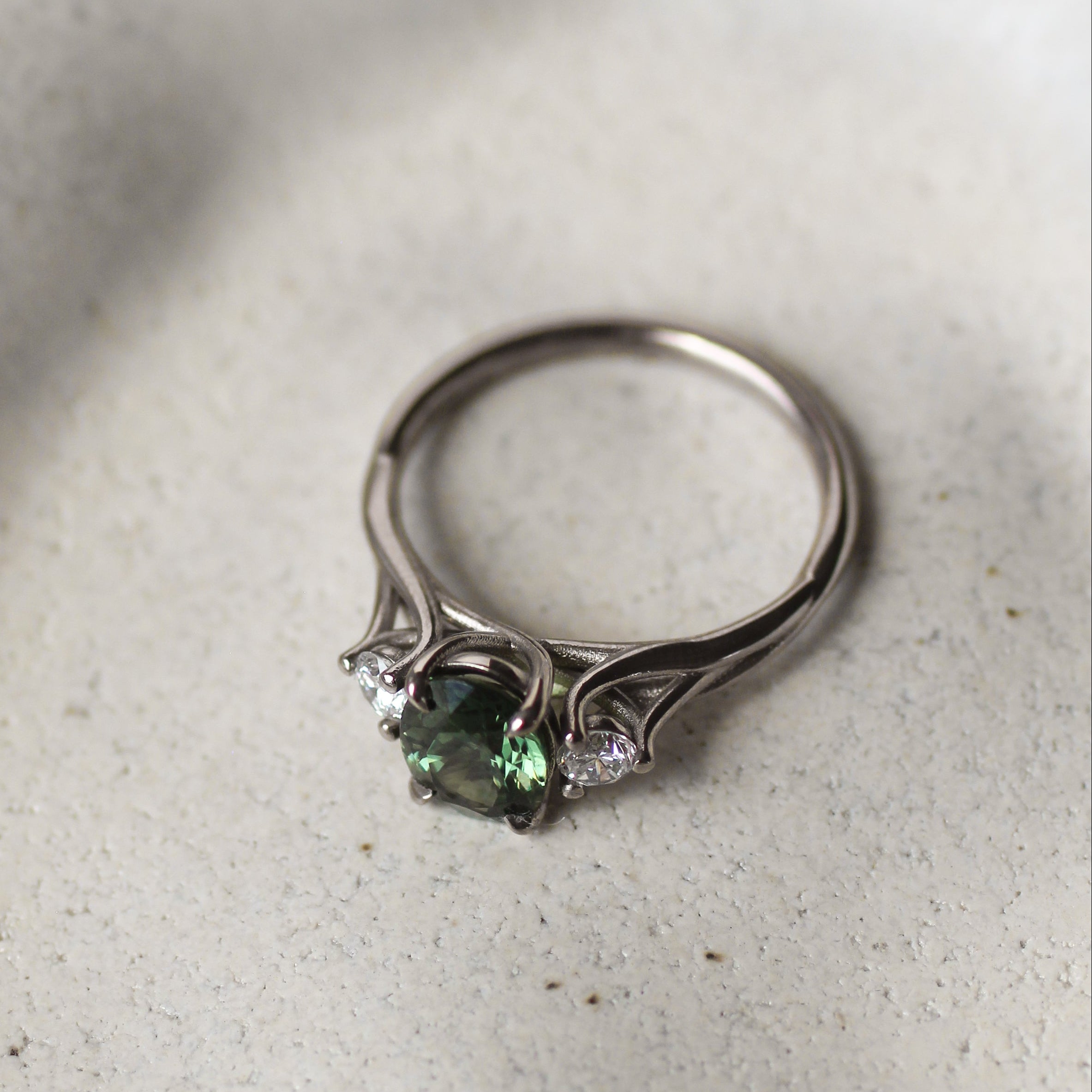 Silver ring with green gemstone on a textured white surface