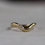 Gold wedding ring with a pear and round diamond on a light fabric background