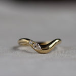 Gold wedding ring with a pear and round diamond on a light fabric background