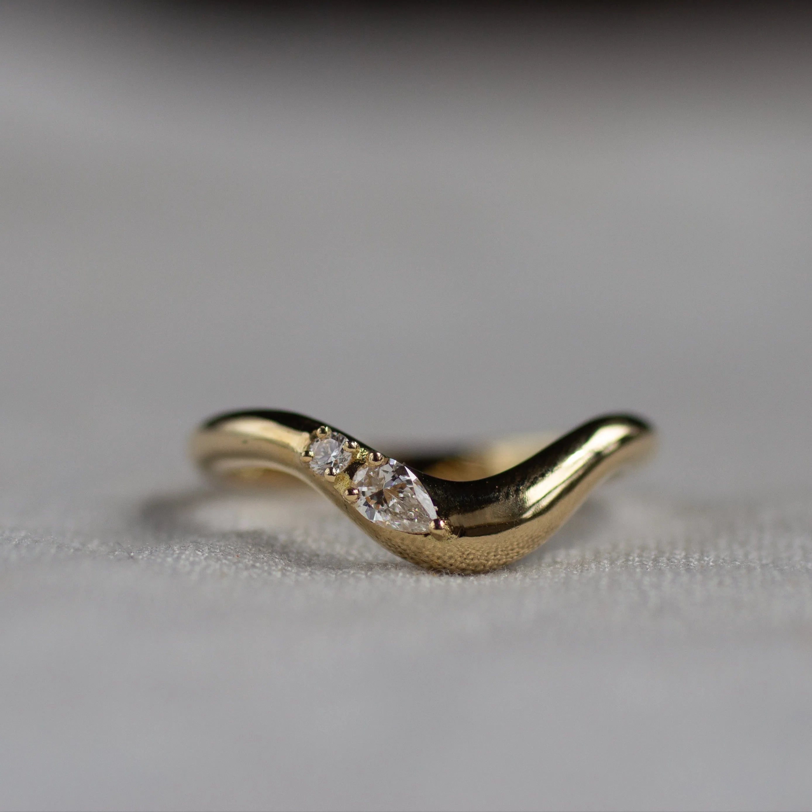Gold wedding ring with a pear and round diamond on a light fabric background