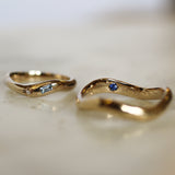 two curved gold wedding rings with blue sapphires, diamonds and engraving with blurred background