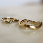 two curved gold wedding rings with blue sapphires, diamonds and engraving with blurred background