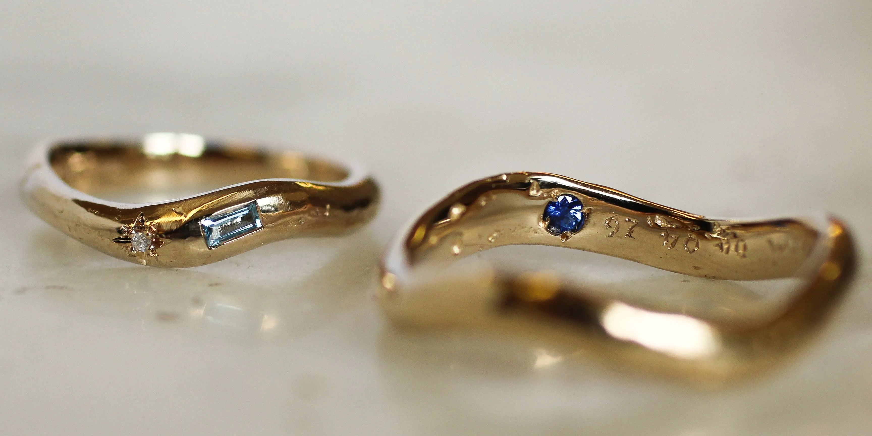 two curved gold wedding rings with blue sapphires, diamonds and engraving with blurred background