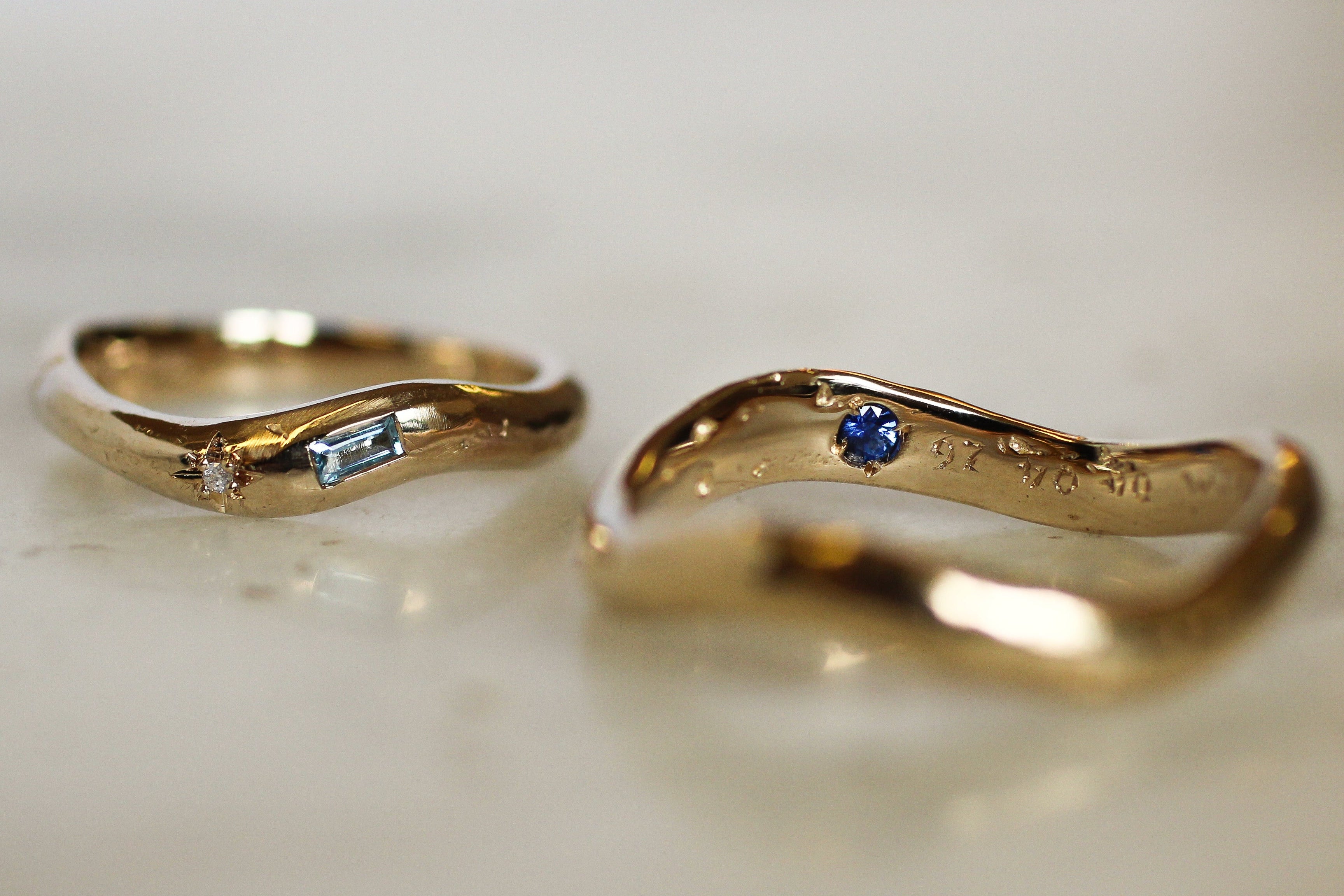 Two gold rings with gemstones on a light background