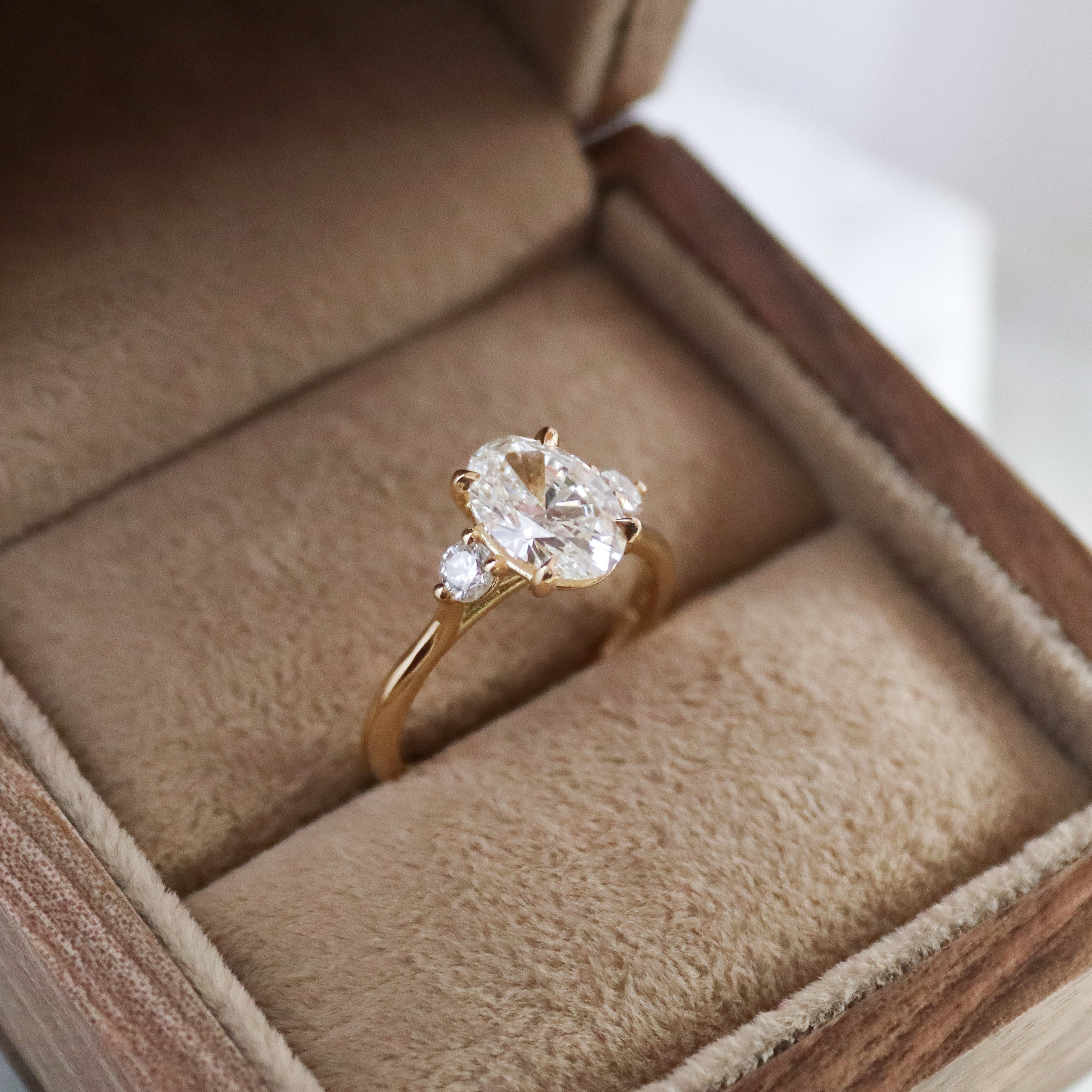 bespoke engagement ring with round and oval diamonds on gold band in ring box