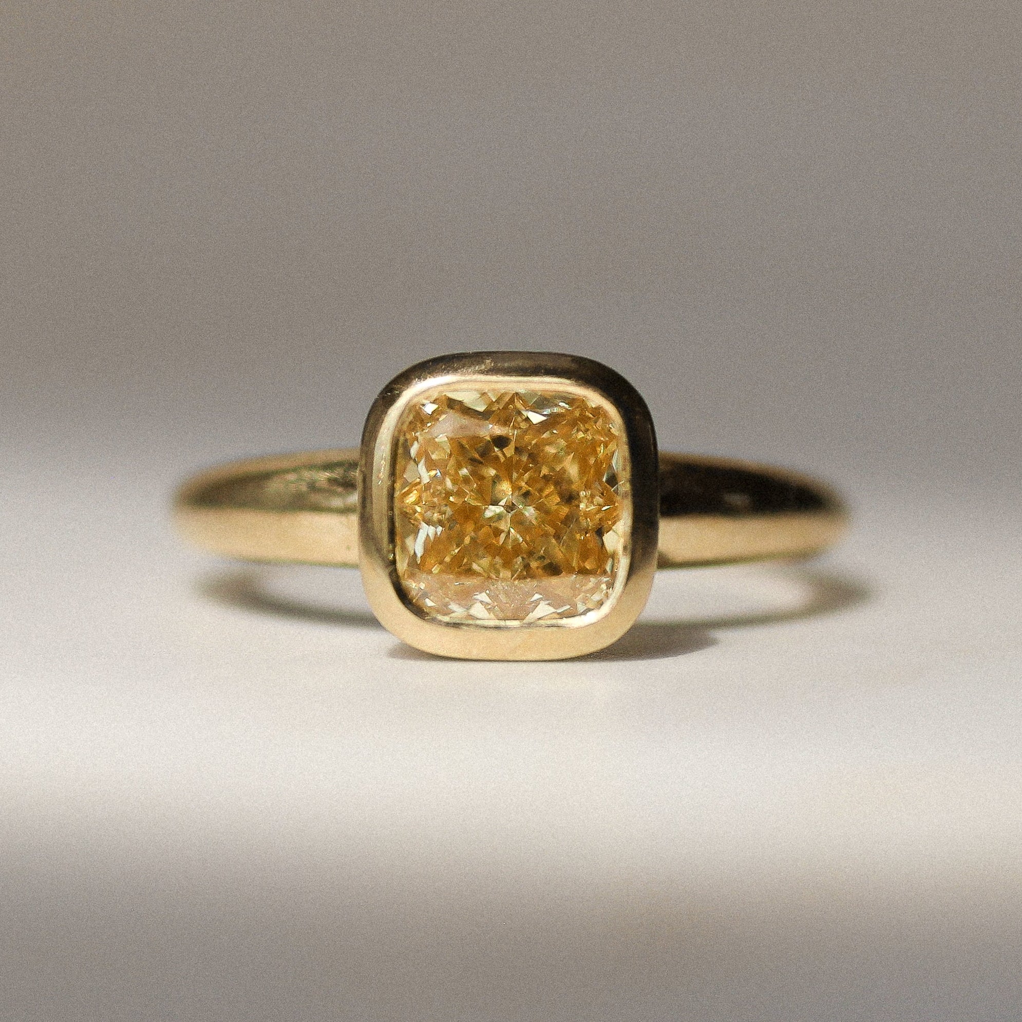 gold bezel set engagement ring with yellow diamond on a neutral surface