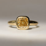 gold bezel set engagement ring with yellow diamond on a neutral surface