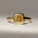 gold bezel set engagement ring with yellow diamond on a neutral surface
