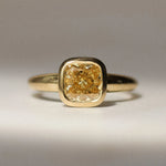 gold bezel set engagement ring with yellow diamond on a neutral surface