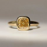 gold bezel set engagement ring with yellow diamond on a neutral surface