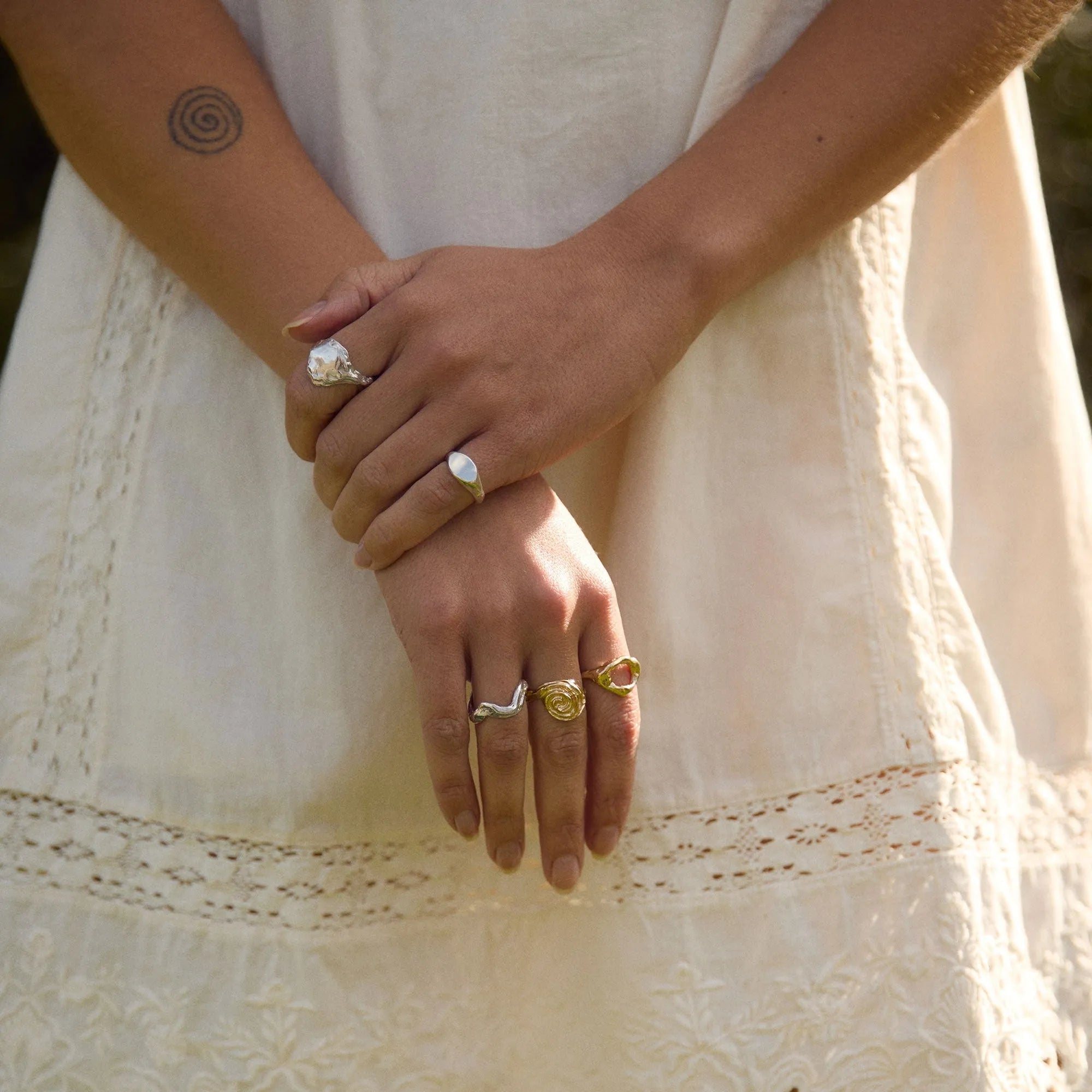 Close-up of hands with rings on a white lace dress against a blurred natural background