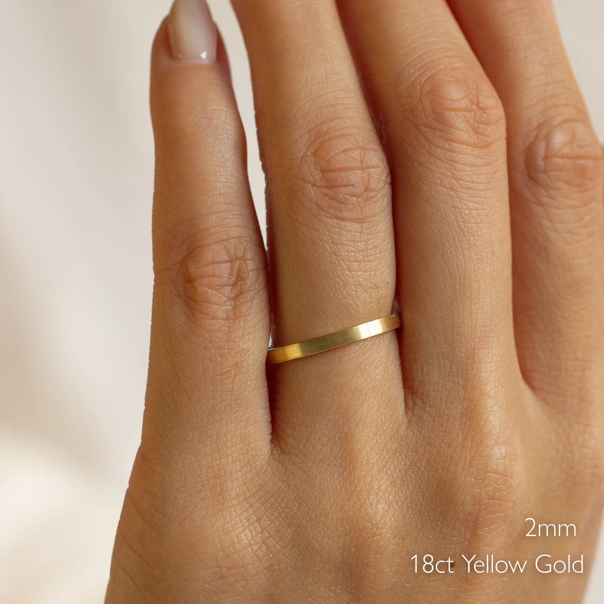 Gold brushed wedding ring in flat on a hand with '2mm 18ct Yellow Gold' text
